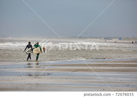 Surfers entering the water in cold windy weather 72076035
