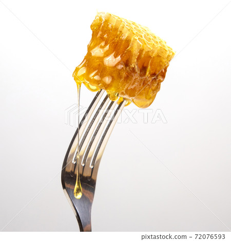 Drops of fresh honey drip from wax honey on a table fork. vitamin nutrition and bee product. Drops of fresh honey drip from wax honey on a table fork. vitamin nutrition and bee product. 72076593