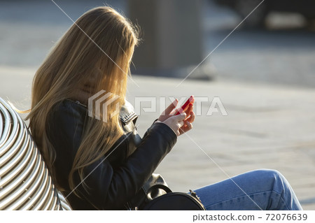 Woman with mobile phone sitting on a bench 72076639