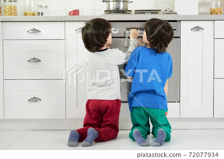 Keep calm. Rear view of curious little hispanic boys, twins watching cake baking in the oven, crouching down in the kitchen Keep calm. Rear view of curious little hispanic boys, twins watching cake baking in the oven, crouching down in the kitchen 72077934