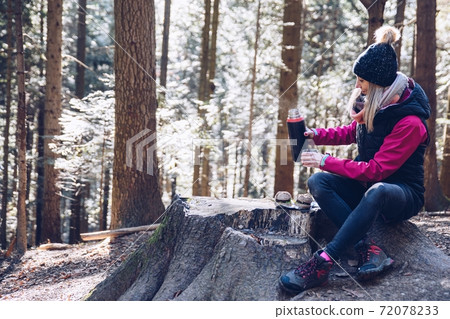 Woman pours hot tea out of thermos into metal cup in autumn forest. 72078233