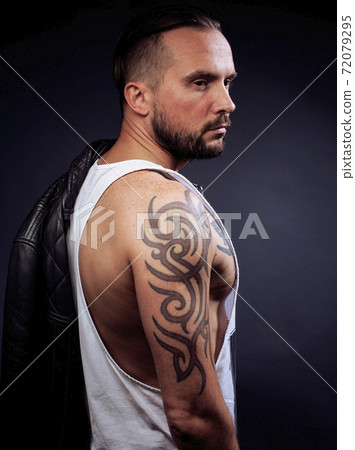 A man with tattooes on his arms. Silhouette of muscular body. caucasian brutal hipster guy with modern haircut, looking like criminal close up A man with tattooes on his arms. Silhouette of muscular body. caucasian brutal hipster guy with modern haircut, looking like criminal close up 72079295