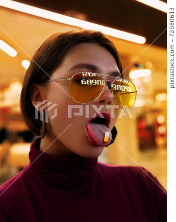 A girl with yellow glasses holding a pill on her tongue 72080613