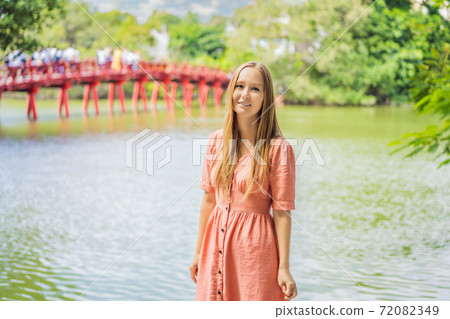 Caucasian woman traveler on background of Red Bridge in public park garden with trees and reflection in the middle of Hoan Kiem Lake in Downtown Hanoi. Vietnam reopens after coronavirus quarantine Caucasian woman traveler on background of Red Bridge in public park garden with trees and reflection in the middle of Hoan Kiem Lake in Downtown Hanoi. Vietnam reopens after coronavirus quarantine 72082349