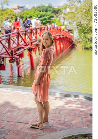 Caucasian woman traveler on background of Red Bridge in public park garden with trees and reflection in the middle of Hoan Kiem Lake in Downtown Hanoi. Vietnam reopens after coronavirus quarantine 72083680
