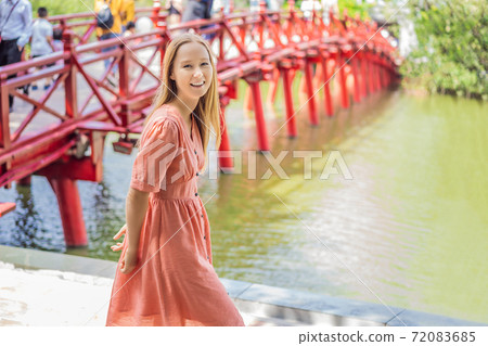 Caucasian woman traveler on background of Red Bridge in public park garden with trees and reflection in the middle of Hoan Kiem Lake in Downtown Hanoi. Vietnam reopens after coronavirus quarantine 72083685