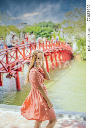 Caucasian woman traveler on background of Red Bridge in public park garden with trees and reflection in the middle of Hoan Kiem Lake in Downtown Hanoi. Vietnam reopens after coronavirus quarantine Caucasian woman traveler on background of Red Bridge in public park garden with trees and reflection in the middle of Hoan Kiem Lake in Downtown Hanoi. Vietnam reopens after coronavirus quarantine 72083692