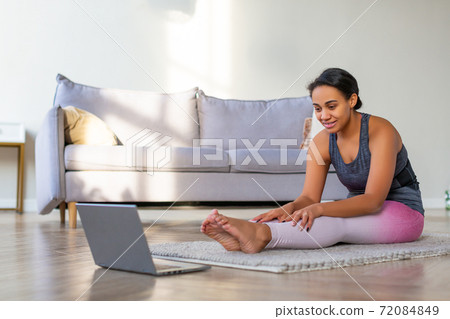 Stretching at home online. African American woman exercising at home in front of a laptop monitor. Stretching at home online. African American woman exercising at home in front of a laptop monitor. 72084849