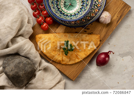 A famous Russian dish is a hot cheburek with meat, vegetables and herbs next to decorative national Uzbek ceramic dishes with a traditional pattern. 72086847