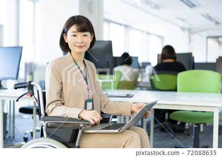 Portrait of a woman in a wheelchair smiling with her laptop on her lap in the office 72088635