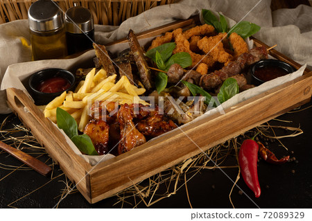 A large set of beer snacks for a company of several people. Plateau with French fries, chicken nuggets, rye garlic croutons, pork ears, chicken legs, kebabs and ketchup. 72089329