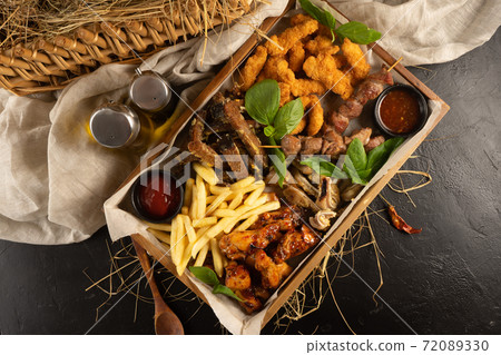 A large set of beer snacks for a company of several people. Plateau with French fries, chicken nuggets, rye garlic croutons, pork ears, chicken legs, kebabs and ketchup. 72089330