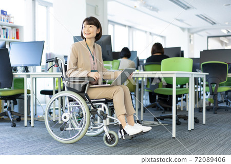 Portrait of a woman in a wheelchair working with her laptop on her lap in the office 72089406
