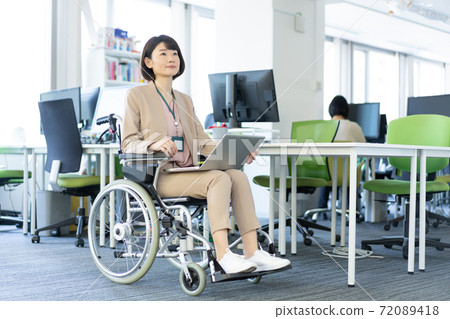 Portrait of a woman in a wheelchair working with her laptop on her lap in the office 72089418