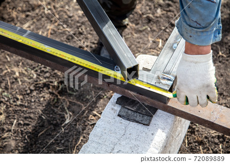 A worker measures metal at a construction site. Technology A worker measures metal at a construction site. Technology 72089889