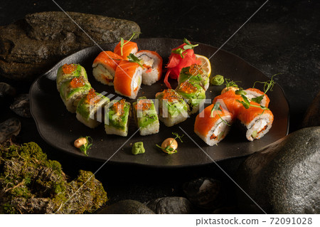 A set of several types of sushi on a beautiful black plate. Japanese dish. Sushi rolls made of salmon, shrimp, avocado, red caviar, rice, ginger, wasabi and peanut sauce. A set of several types of sushi on a beautiful black plate. Japanese dish. Sushi rolls made of salmon, shrimp, avocado, red caviar, rice, ginger, wasabi and peanut sauce. 72091028