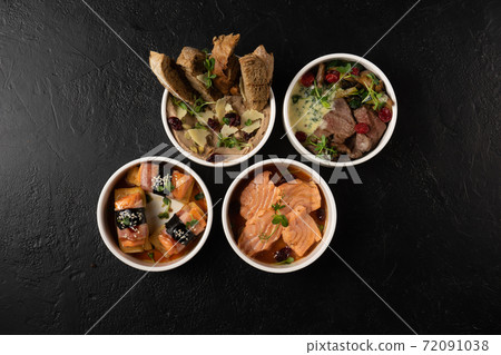 A set of four hot and cold appetizers of meat and fish. Salmon, Japanese bacon omelet, bread and cheese pate and beef in a creamy sauce. 72091038
