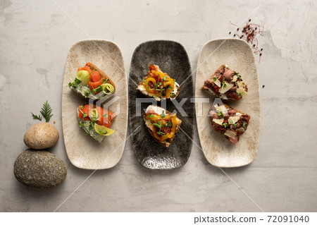 A set of three different types of bruschetta. Bruschetta with salmon and green butter, vegetables and cream cheese, bacon and sun-dried tomatoes. 72091040