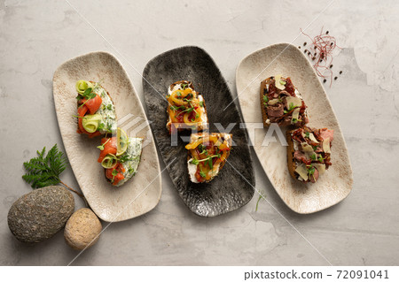 A set of three different types of bruschetta. Bruschetta with salmon and green butter, vegetables and cream cheese, bacon and sun-dried tomatoes. 72091041