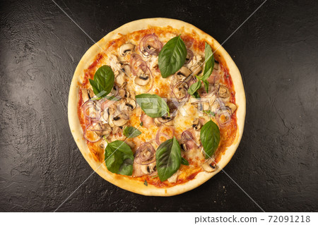 Round hot freshly baked pizza with mushrooms, chicken, basil, onions and cheese lies on a black stone kitchen table Round hot freshly baked pizza with mushrooms, chicken, basil, onions and cheese lies on a black stone kitchen table 72091218