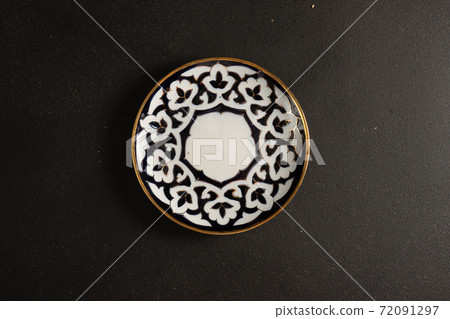 Ethnic Uzbek ceramic tableware on the black background. Decorative ceramic plate with traditional ornament. 72091297
