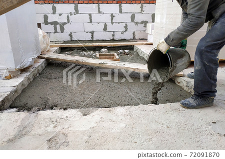 auxiliary worker pours out of a bucket liquid cement mortar on the floor between the floors of the house auxiliary worker pours out of a bucket liquid cement mortar on the floor between the floors of the house 72091870