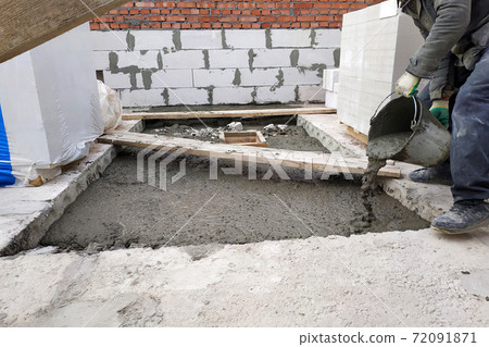The builder pours a cement mortar slab between the floors of the house using a bucket The builder pours a cement mortar slab between the floors of the house using a bucket 72091871