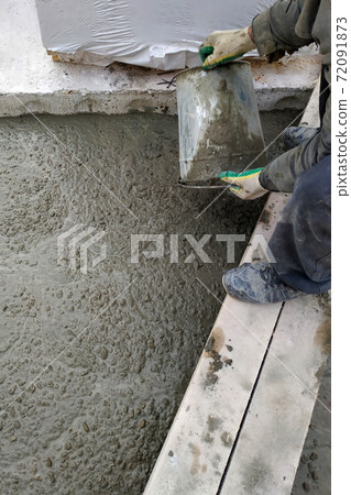 The builder pours a cement mortar slab between the floors of the house using a bucket The builder pours a cement mortar slab between the floors of the house using a bucket 72091873