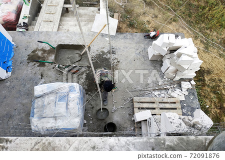 The worker collects a cement mortar in a carriage bucket on the construction site 72091876