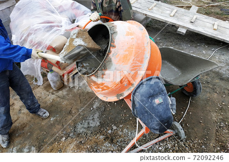 auxiliary worker develops a cement mortar in a concrete mixer at the construction of a country house 72092246