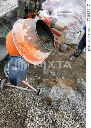 auxiliary worker develops a cement mortar in a concrete mixer at the construction of a country house 72092247