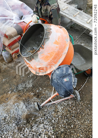 auxiliary worker develops a cement mortar in a concrete mixer at the construction of a country house 72092248