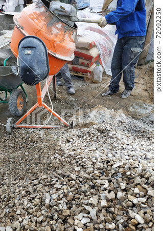 auxiliary worker develops a cement mortar in a concrete mixer at the construction of a country house auxiliary worker develops a cement mortar in a concrete mixer at the construction of a country house 72092250