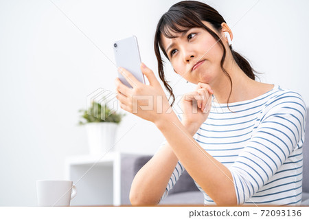 A woman who operates a smartphone while relaxing on the sofa. 72093136