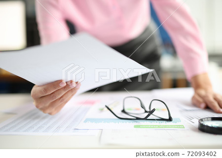 Female hands hold documents on table are commercial charts and magnifying glass. 72093402