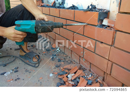 The builder dismantles the brick in the wall with a punch The builder dismantles the brick in the wall with a punch 72094865