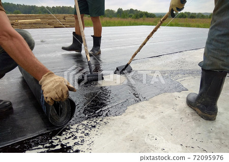 Roofer worker painting bitumen praimer at concrete surface by the roller brush Waterproofing 72095976