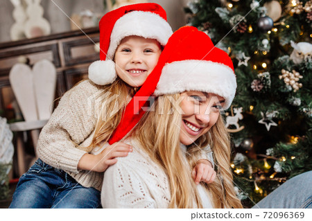 Portrait of happy mother in santa claus and daughter near christmas tree at home. Merry Christmas 72096369