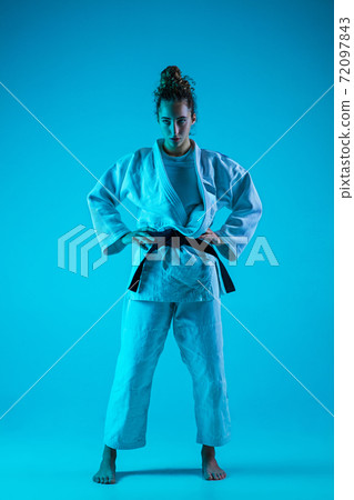 Portrait of professional female judoist isolated on blue studio background in neon light. Healthy lifestyle, sport concept. Portrait of professional female judoist isolated on blue studio background in neon light. Healthy lifestyle, sport concept. 72097843