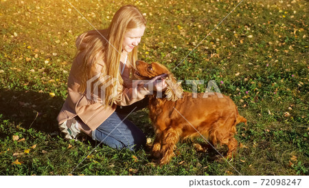 Teenager girl with long loose fair hair pets and kisses dog 72098247