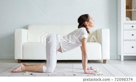 Pregnant lady does marjaryasana on floor near sofa at home Pregnant lady does marjaryasana on floor near sofa at home 72098374