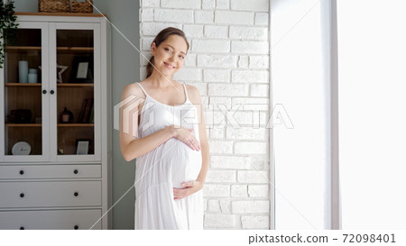 Future mother touches tummy standing near brick wall in room Future mother touches tummy standing near brick wall in room 72098401