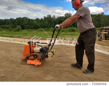Soil compaction by a worker with a vibroplate Soil compaction by a worker with a vibroplate 72099448