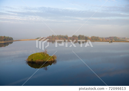 Still water of a reservoir acts as a mirror reflecting a winter sky. Still water of a reservoir acts as a mirror reflecting a winter sky. 72099813