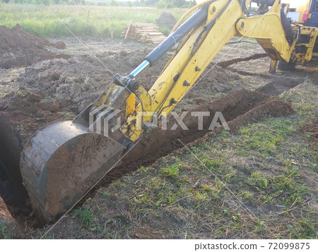 A work excavator digs a trench in a country house A work excavator digs a trench in a country house 72099875