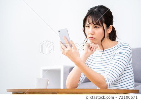 一個女人在客廳裡放鬆的同時操作智能手機。 一個女人在客廳裡放鬆的同時操作智能手機。 72100671