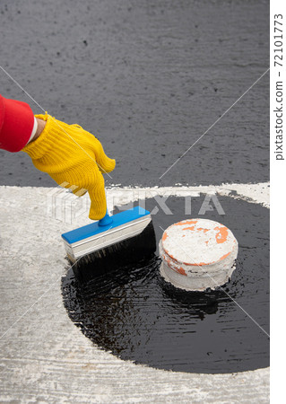 Worker applies bitumen mastic on the foundation 72101773