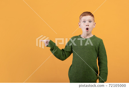 Excited ginger boy in green sweater pointing at copy space Excited ginger boy in green sweater pointing at copy space 72105000