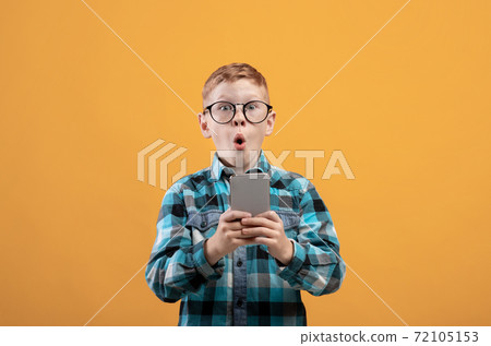 Surprised schoolboy playing game on smartphone, yellow background 72105153