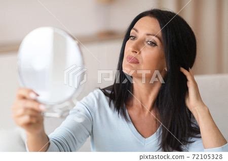Adult woman checking her face in mirror Adult woman checking her face in mirror 72105328